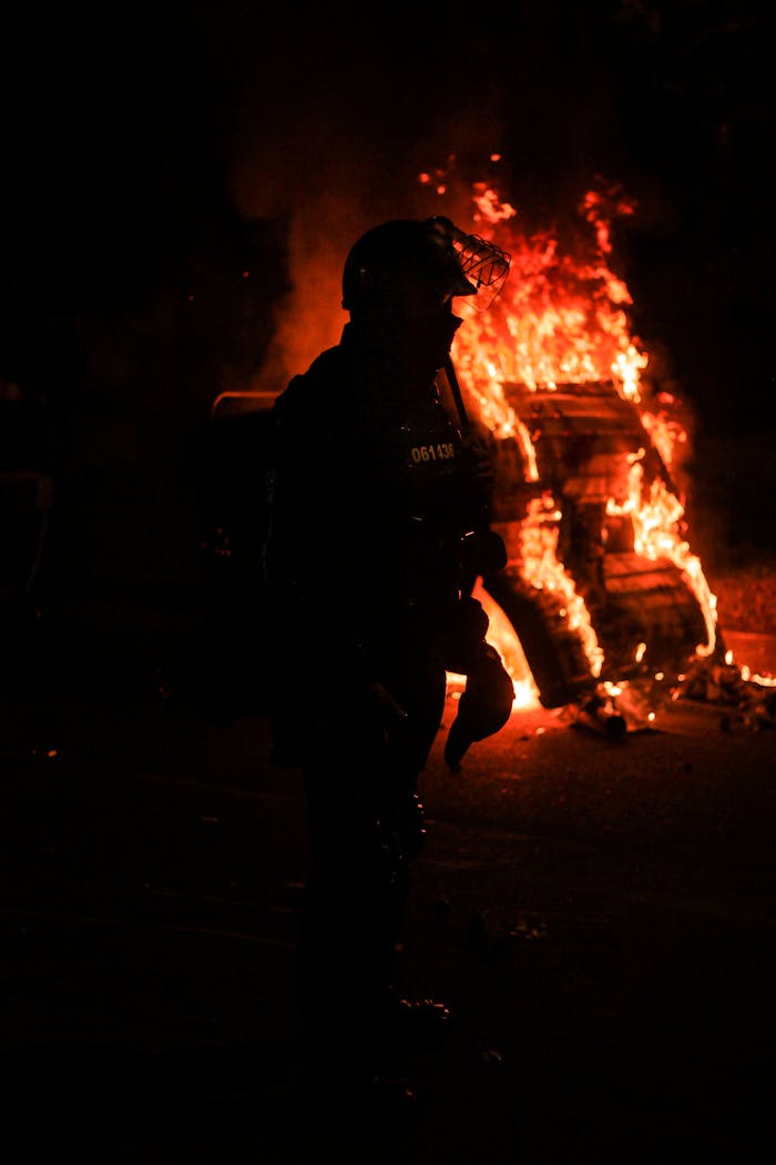 A tense night scene in Bogotá with a silhouette of a police officer against a fire backdrop during protests.